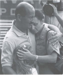 Photograph of Commander Barbara Vernoski hugging her husband and daughter before boarding the USNS Comfort in 1990.