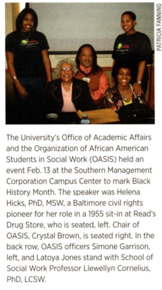 Color newspaper clipping of a group of people, two people are standing, three people are sitting