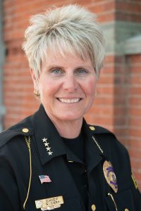 Color photograph of a woman with short blond hair in a police uniform, the woman is smiling