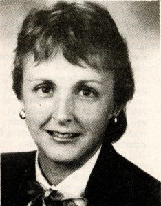 Black and white photograph of a woman, she has short hair and is smiling at the camera