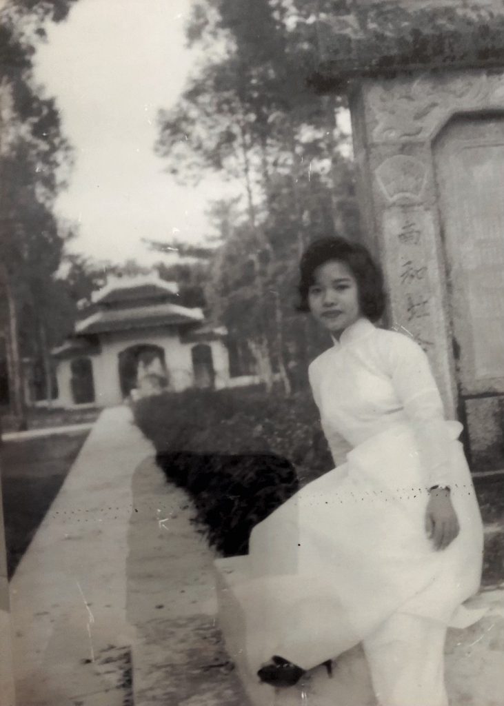 Black and white photograph of a woman in a wedding dress sitting in front of a garden.
