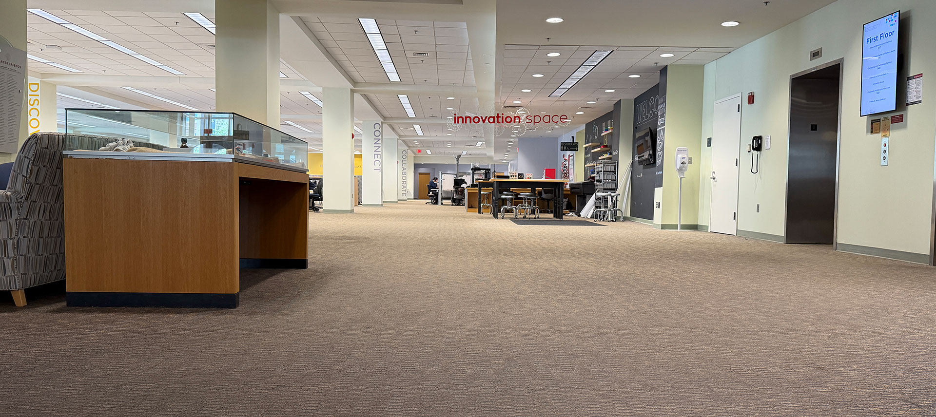 Interior of an academic workspace with carpeted floors, display case, worktables, and innovation space signage.