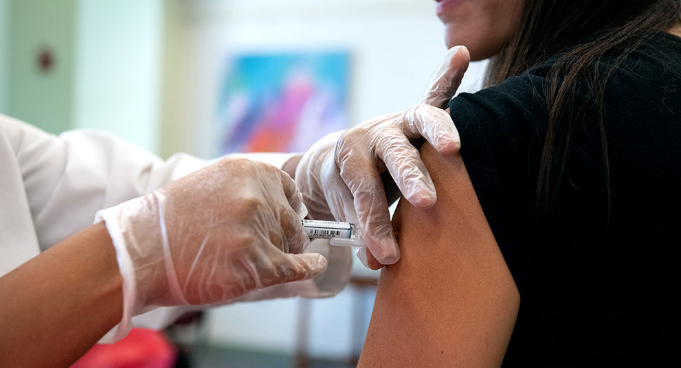 Gloved healthcare worker administering an injection into a person’s upper arm.