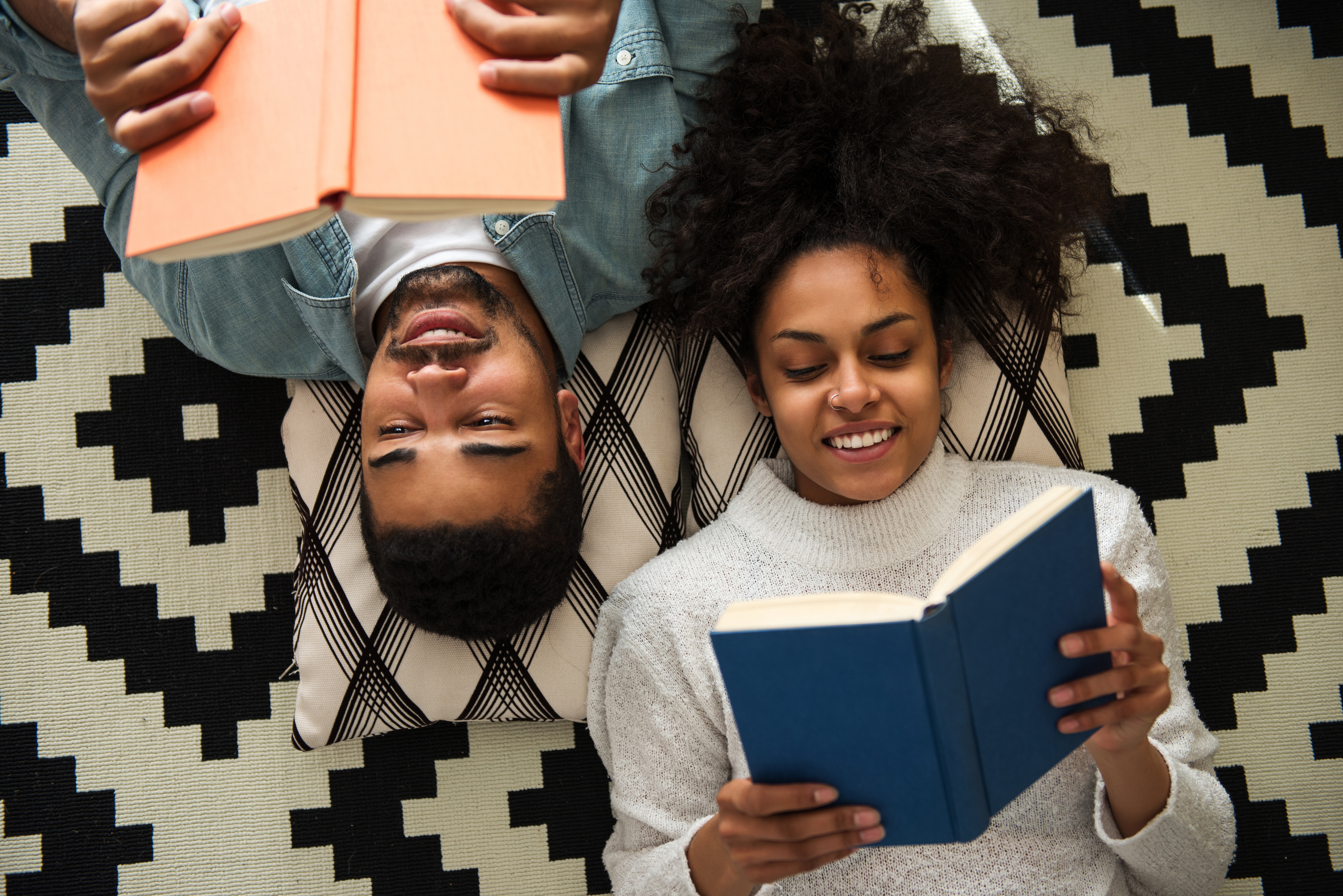 African american couple lying on the floor and reading books.