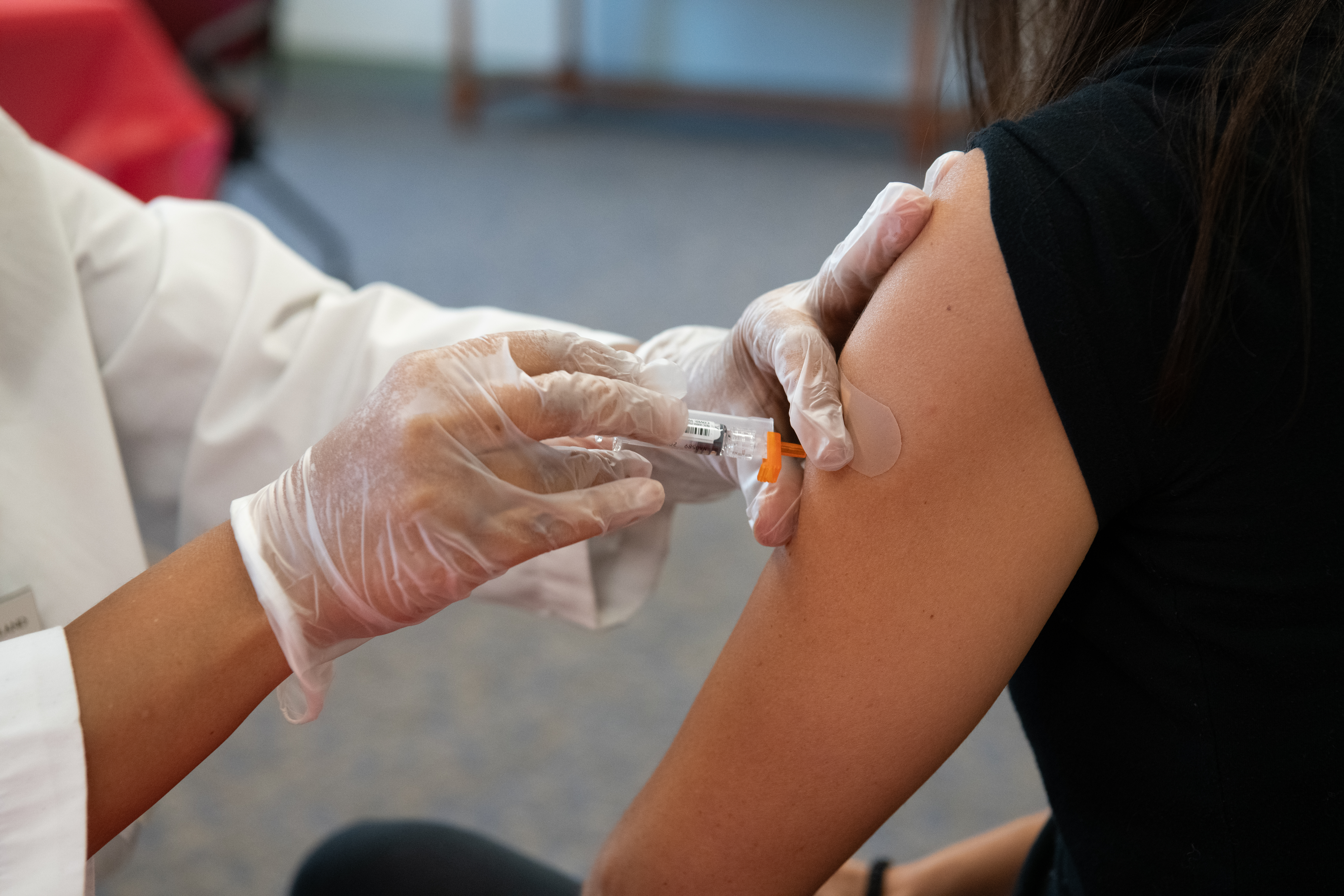 Photograph showing a healthcare professional wearing gloves administering a vaccine injection into a person's upper arm. 