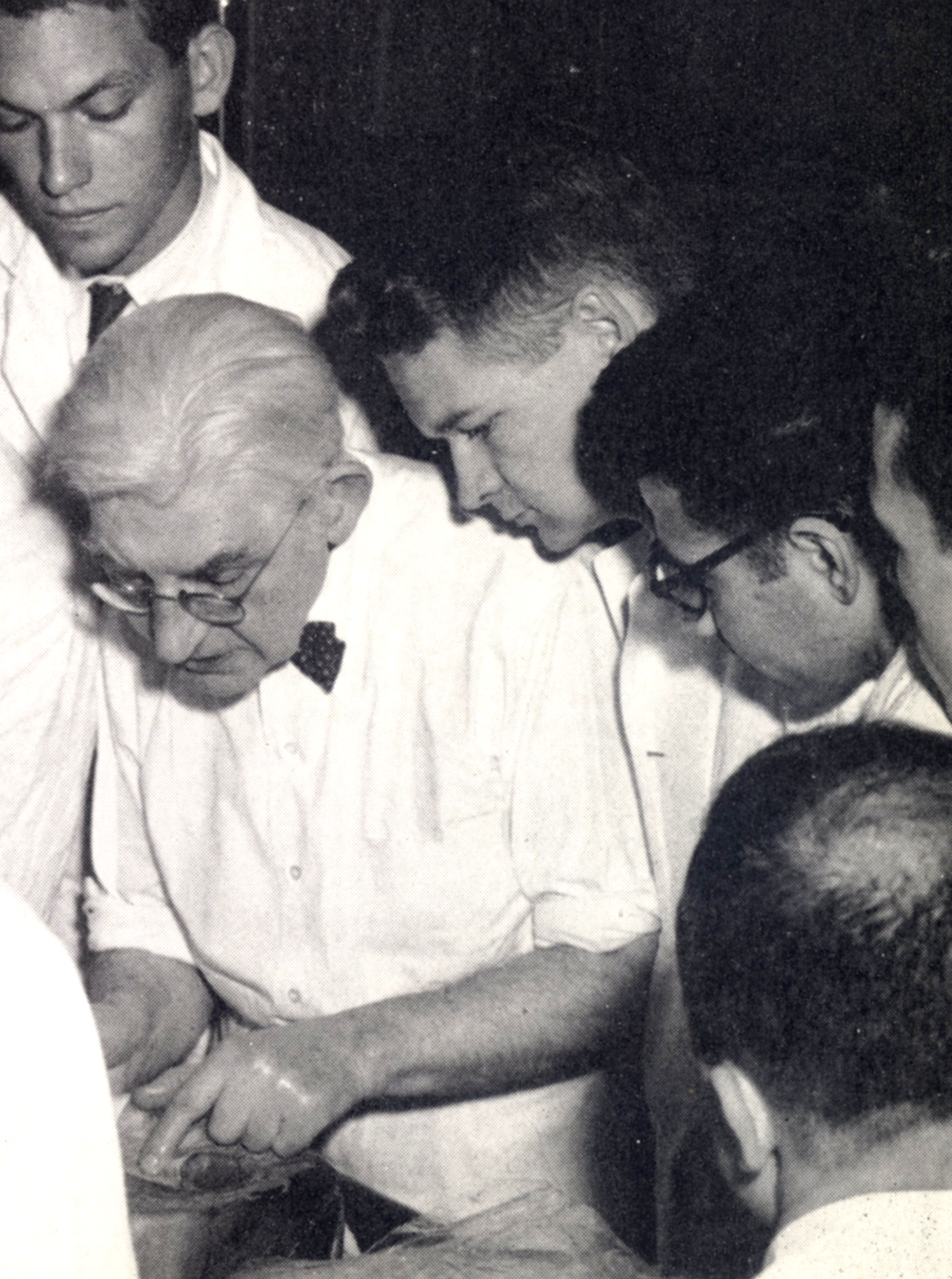 Black-and-white photograph of several people gathered around and examining a person lying in the foreground.